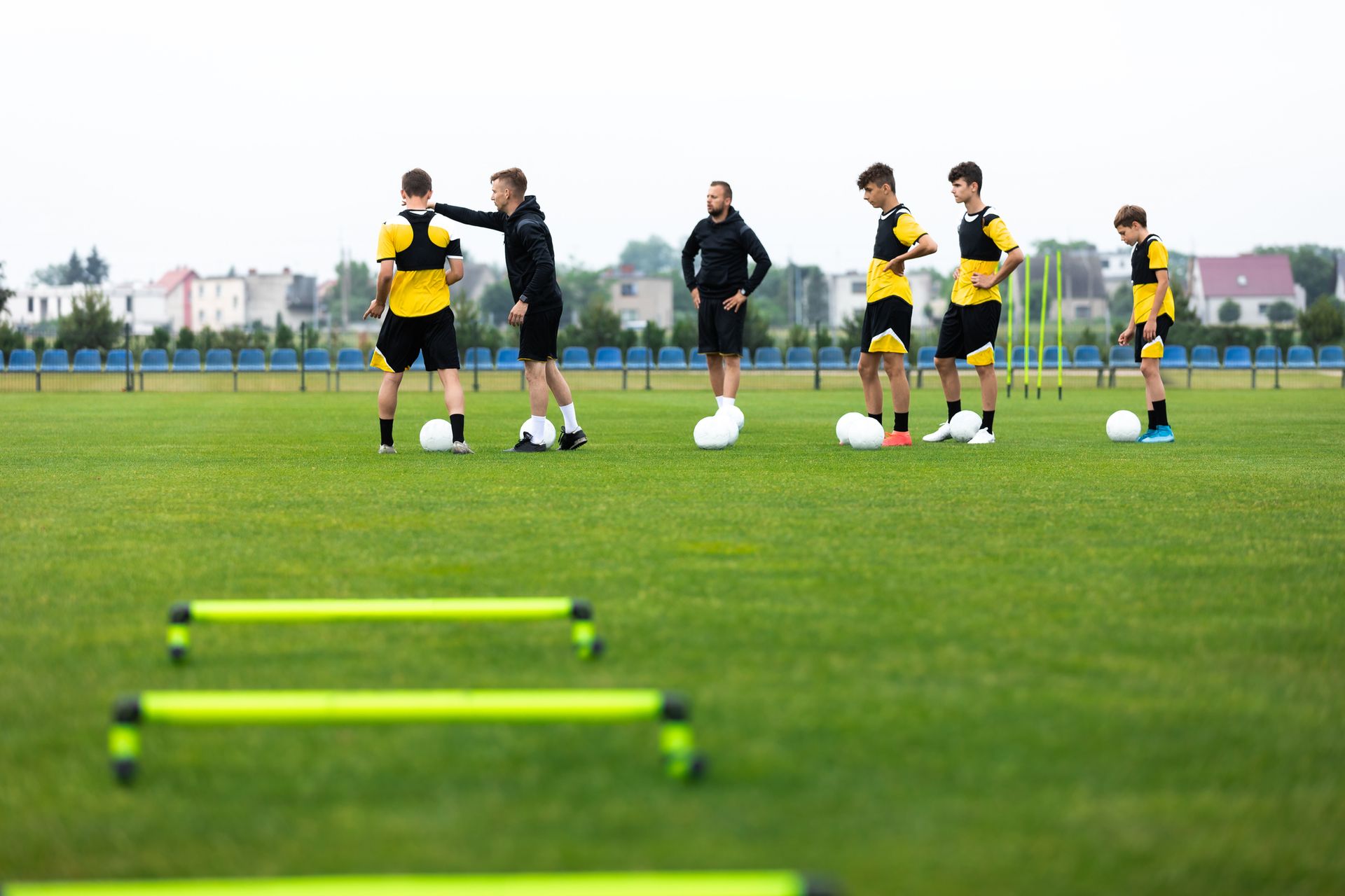 Young soccer players and a coach stand on a field beside low hurdles and cones.
