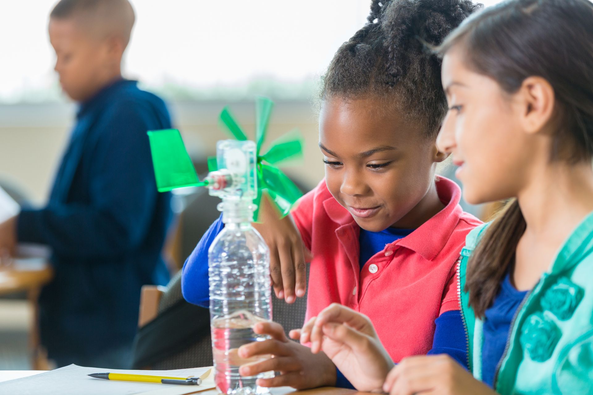 Children build a small windmill from a plastic bottle at a classroom table.