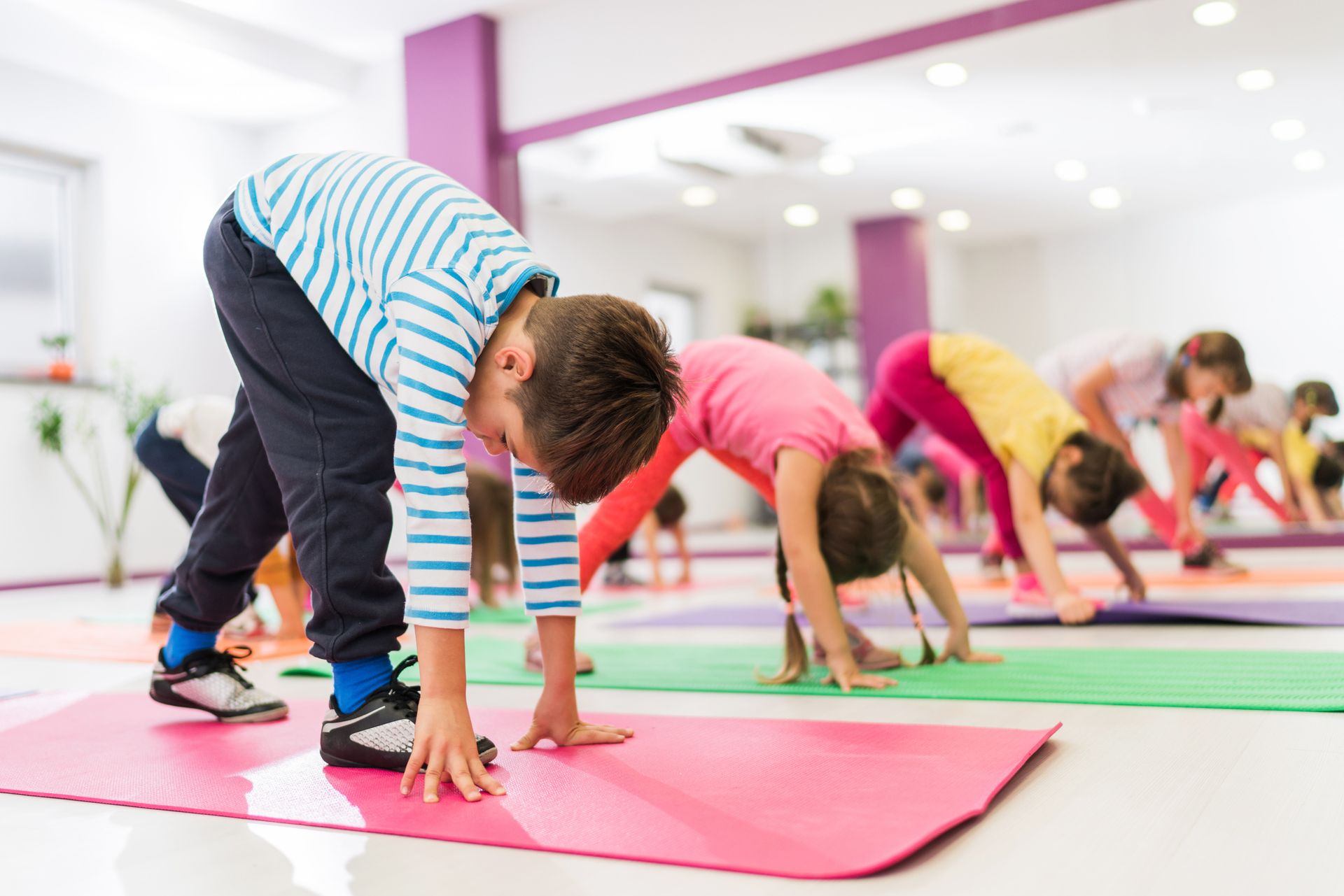 Children stretch down to touch their toes on colorful exercise mats in a bright room.